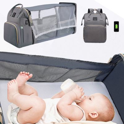 Baby lying on a portable crib with a diaper bag and baby bottle nearby.